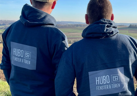 Zwei HUBO Mitarbeiter in dunkelblauen Firmenpullovern mit HUBO Logo betrachten die Landschaft im Saarland - Professionelle Handwerker für Fenster und Türen in Lebach